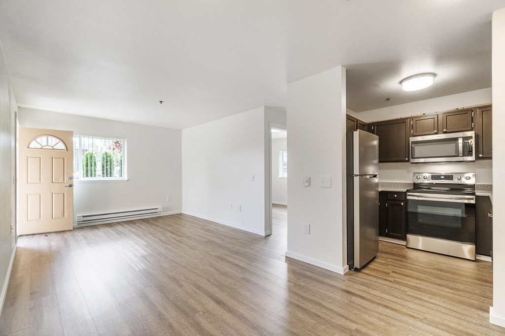 an empty living room and kitchen with stainless steel appliances and wood flooring