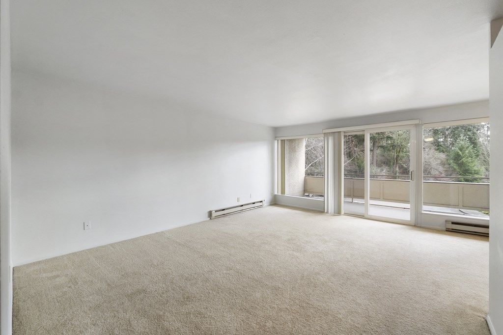 an empty living room with large windows and a carpeted floor