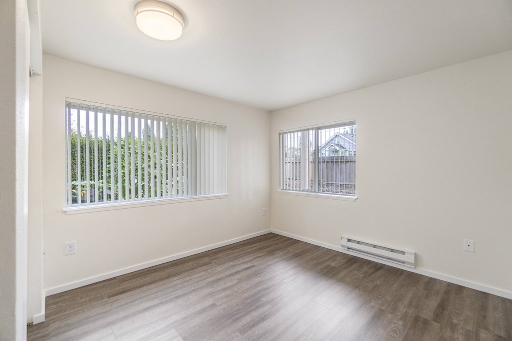 an empty living room with wood flooring and two windows