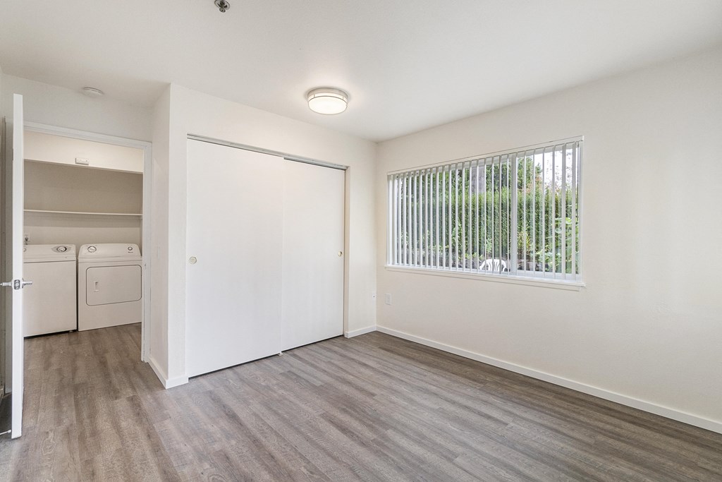 the living room and laundry room of an apartment with white walls and wood flooring