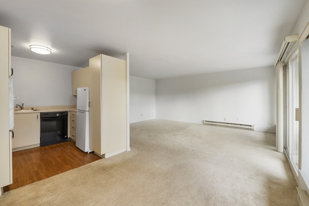the living room and kitchen of an apartment with white walls and wood flooring