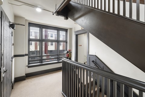 A black metal staircase with a white wall and a window with a view of a building.