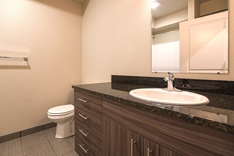 A bathroom with a white toilet, brown drawers, and a white sink.