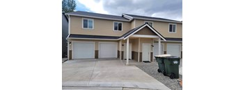 a beige house with white garage doors and a gravel driveway