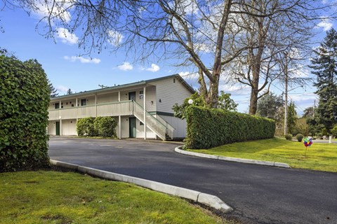 A building with a grey roof and white walls is surrounded by greenery.