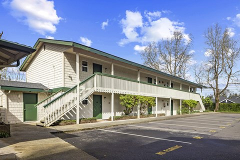 A white building with green doors and windows is surrounded by a parking lot.