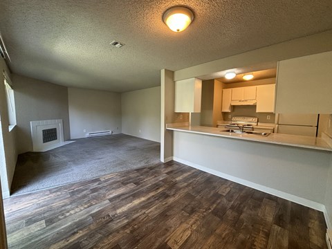 A room with wooden flooring and a kitchen area in the background.