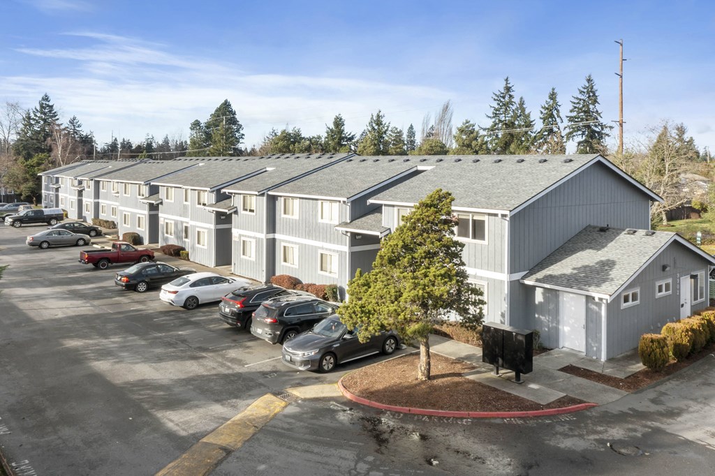 a parking lot in front of an apartment building with cars and a cow