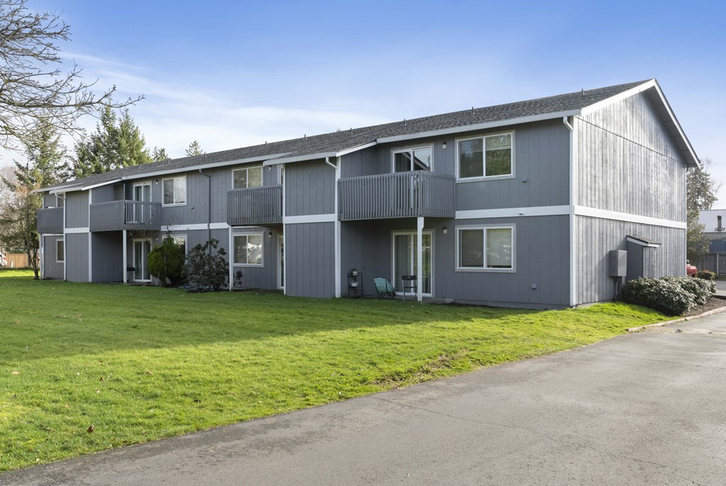 a gray building with a green lawn and a road