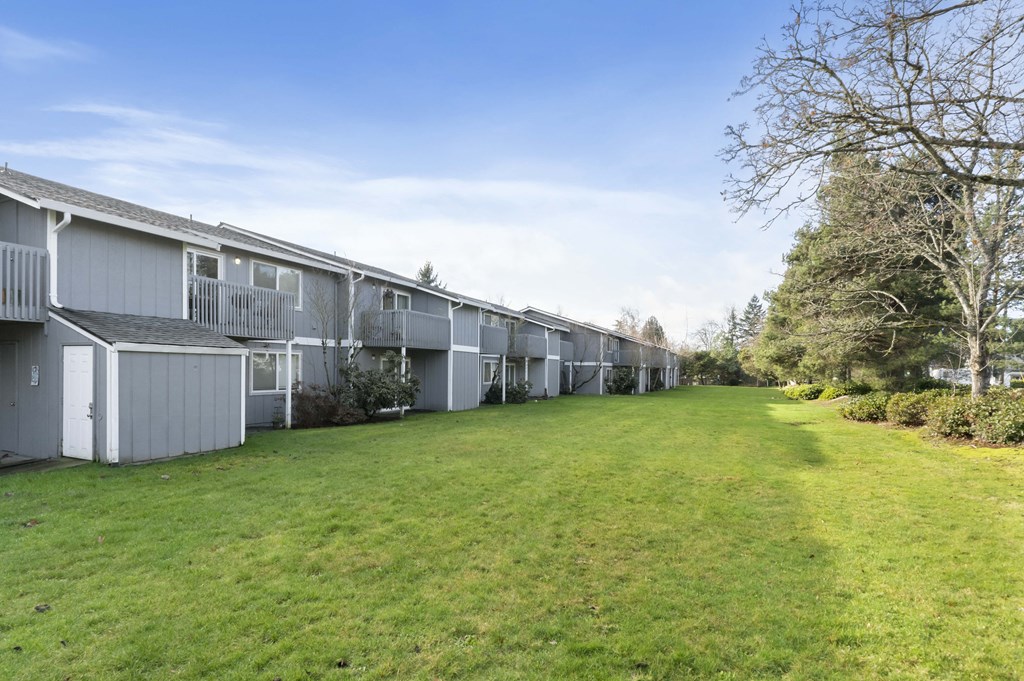 a row of condominiums with a green lawn and trees
