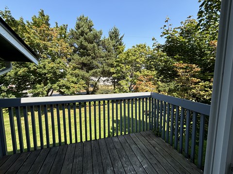 A wooden deck with a railing overlooking a grassy area.