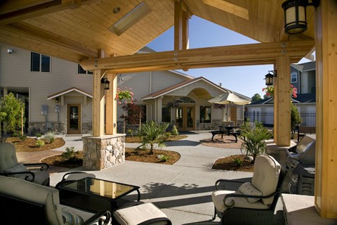 A wooden pergola with a glass table and chairs is in the foreground of a residential area.