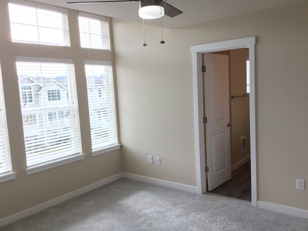 a bedroom with two large windows and a door to a closet