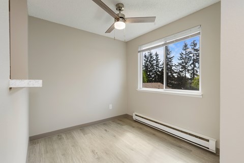 A dining room with a window showing trees outside and wood plank flooring.
