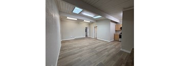 an empty living room with wood flooring and a kitchen