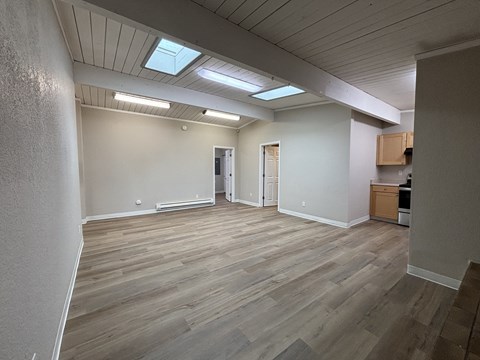 an empty living room with wood flooring and a kitchen
