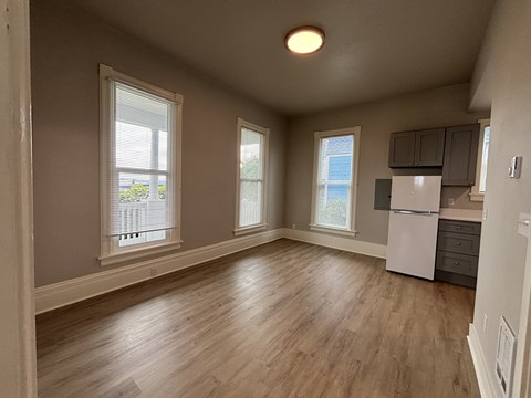 A spacious room with wooden floors and a white refrigerator.