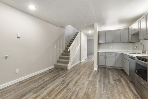 the kitchen and living room of a new home with gray cabinets and a staircase