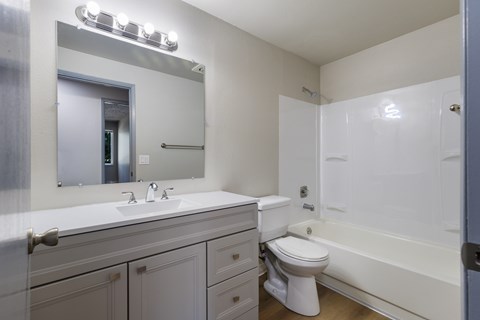 A white bathroom with a sink, mirror, toilet and bathtub.