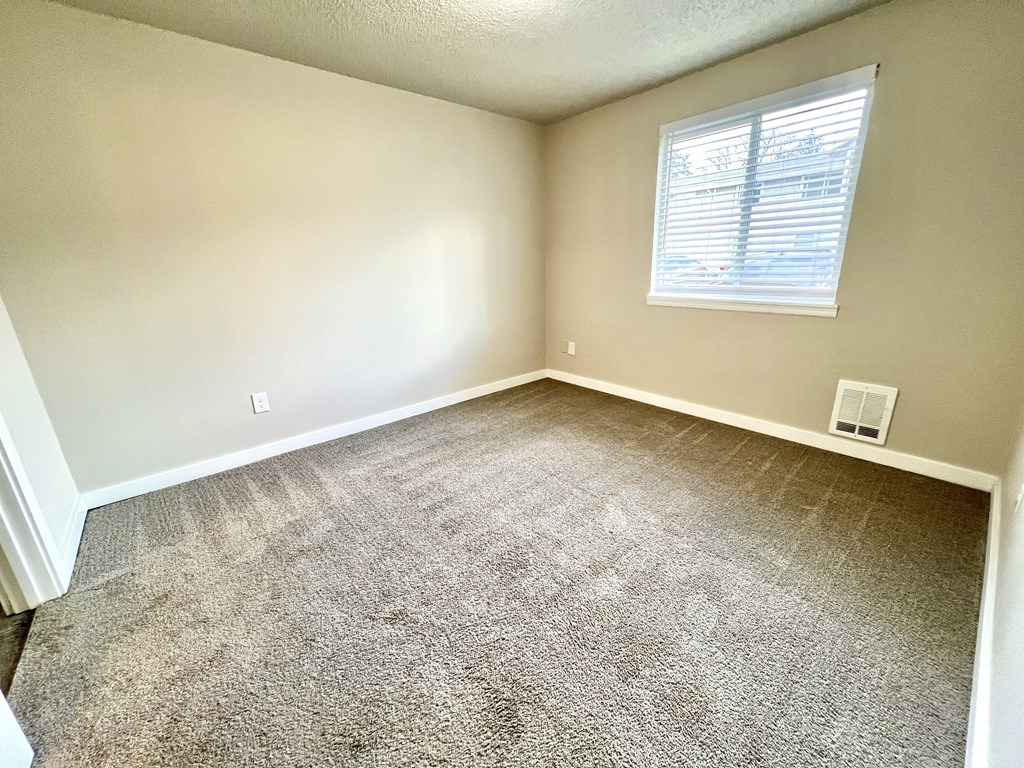 A room with a carpeted floor and a window with blinds.