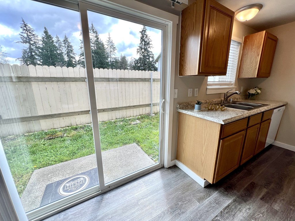A kitchen with a wooden cabinet and a window overlooking a fence.