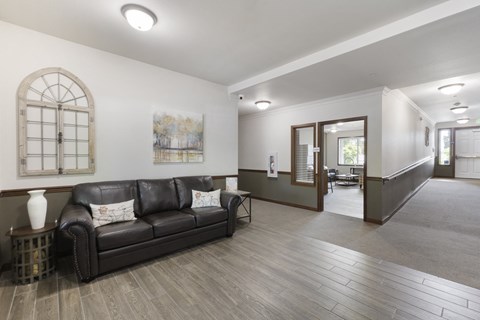 A black leather couch sits in a spacious room with wood flooring and a large window.