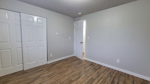 A room with wooden floors and white walls with three doors.