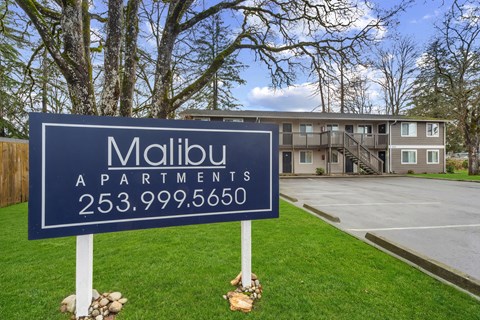A blue sign for Malibu Apartments stands in front of a building.