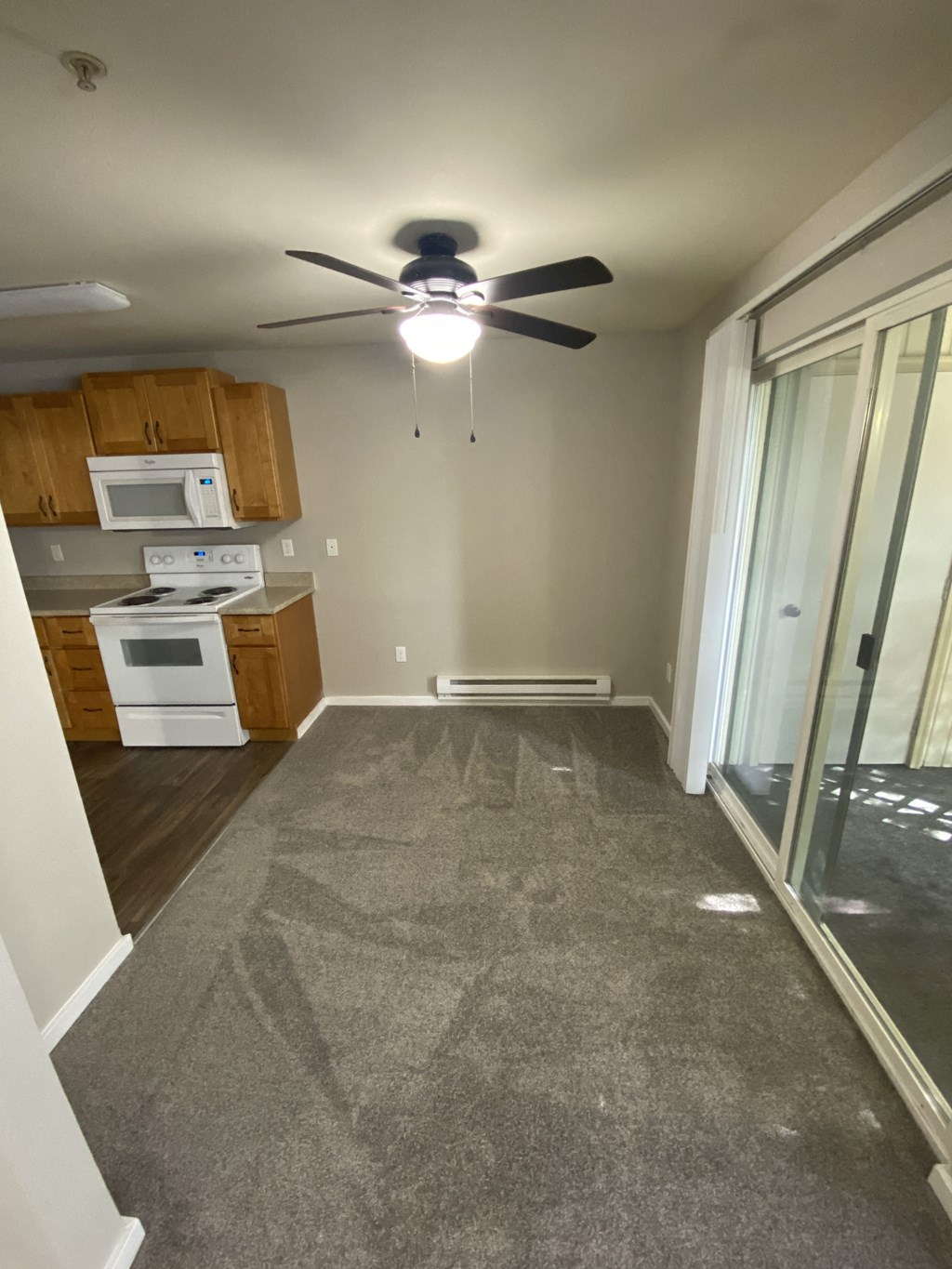 an empty living room with a ceiling fan and a kitchen