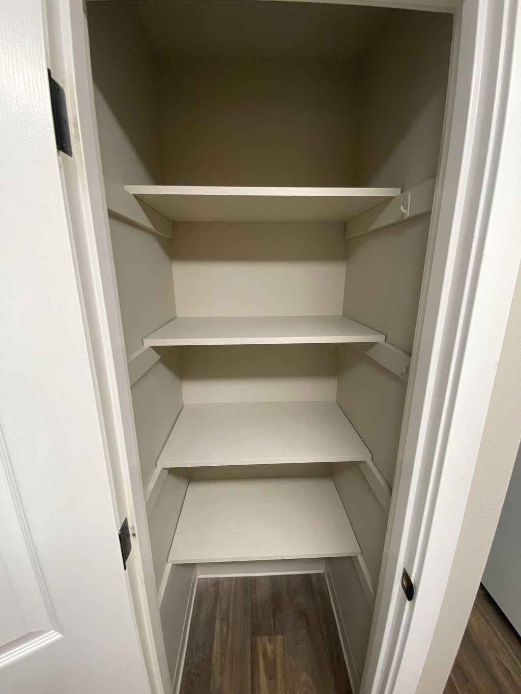 a walk in closet with white shelves and a wood floor