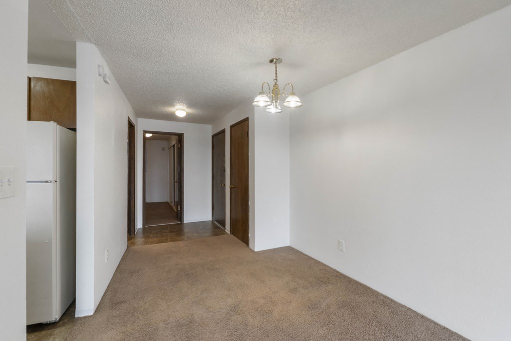 a spacious living room with white walls and carpeting and a door to a hallway