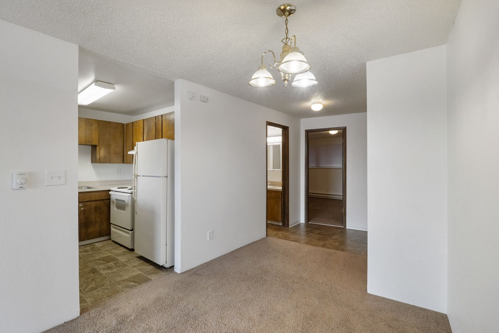 an empty living room with a kitchen and a white refrigerator