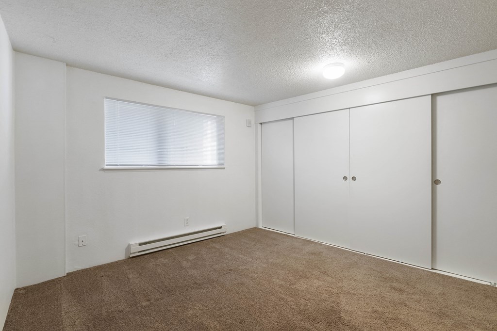 an empty living room with white walls and carpet and a window