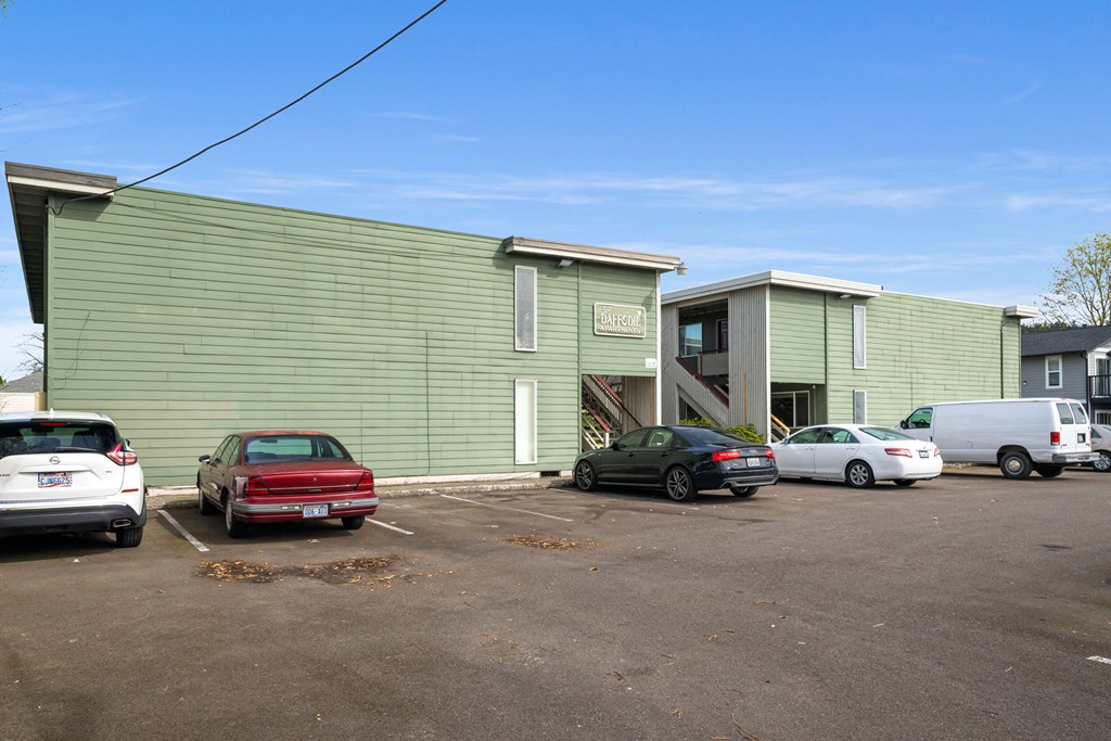 A parking lot with cars and a green building in the background.