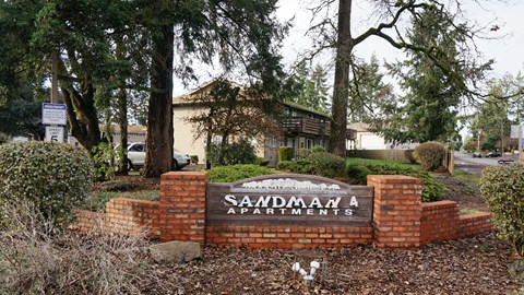A sign for Saadman Apartments is surrounded by a brick wall and shrubbery.