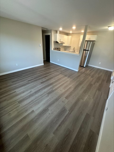 A room with wooden flooring and a kitchen area in the background.