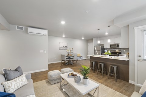 A modern living room with a grey couch, a white coffee table, and a kitchen area in the background.