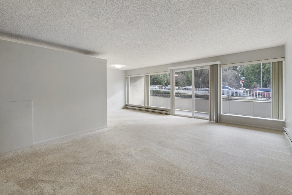 the living room and dining room of an apartment with large windows and carpeting