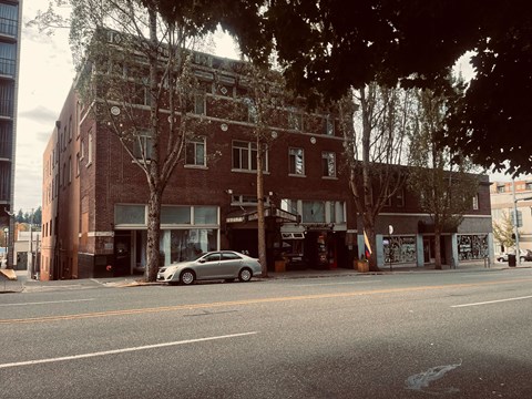 A silver car is parked on the side of a street in front of a brick building.