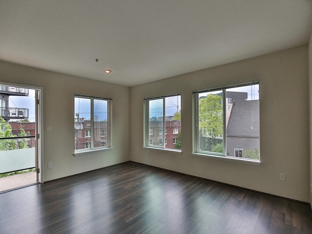an empty living room with a wood floor and three windows