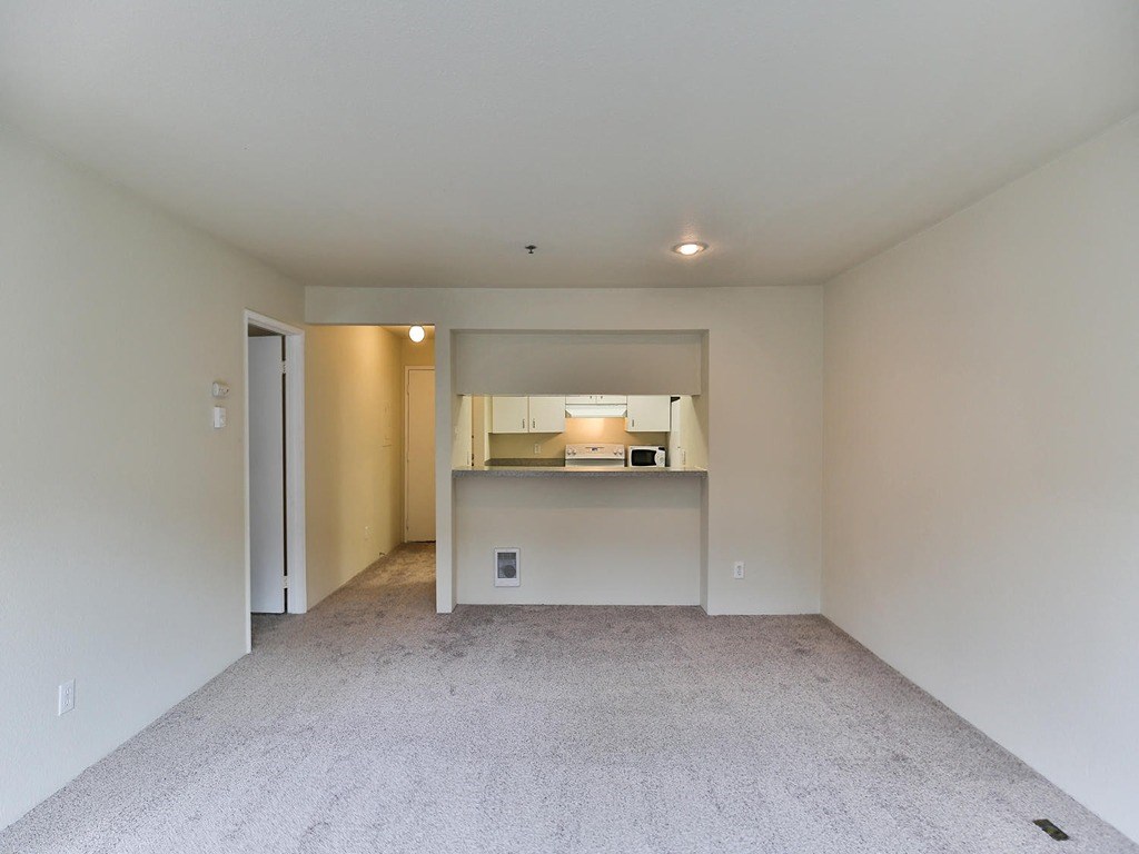 an empty living room with a kitchen in the distance