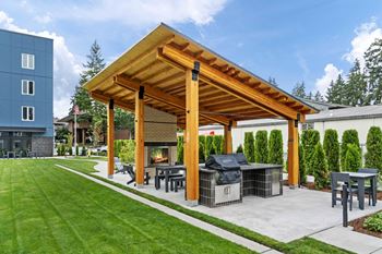 A wooden pergola with a grill and seating area in a backyard.