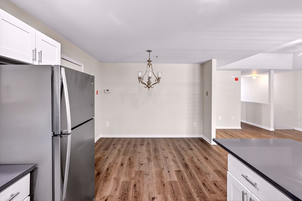 A kitchen with a refrigerator, wooden floors, and a chandelier.