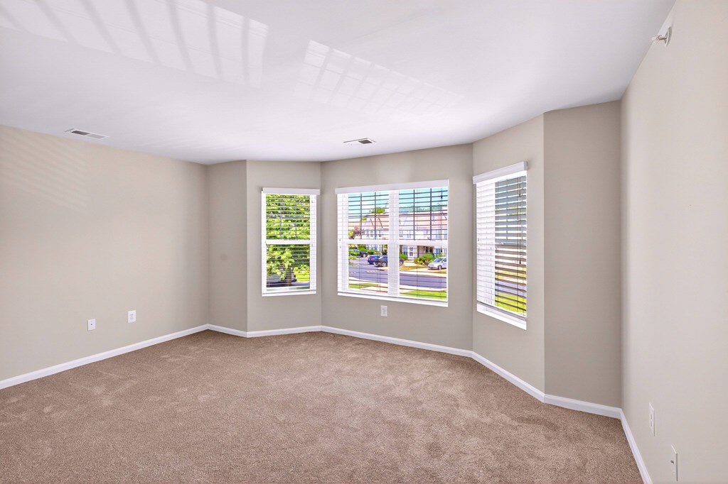A room with a carpeted floor and two windows with blinds.