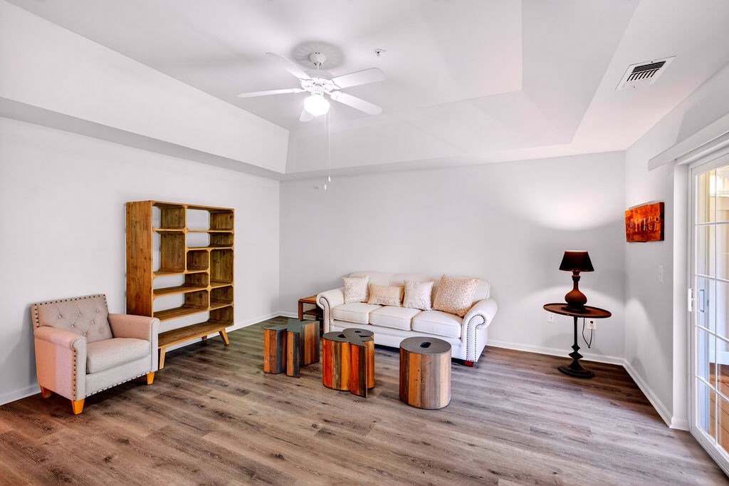 A living room with a white couch, a wooden chair, a wooden shelf, a round table with a lamp, and a white rug.
