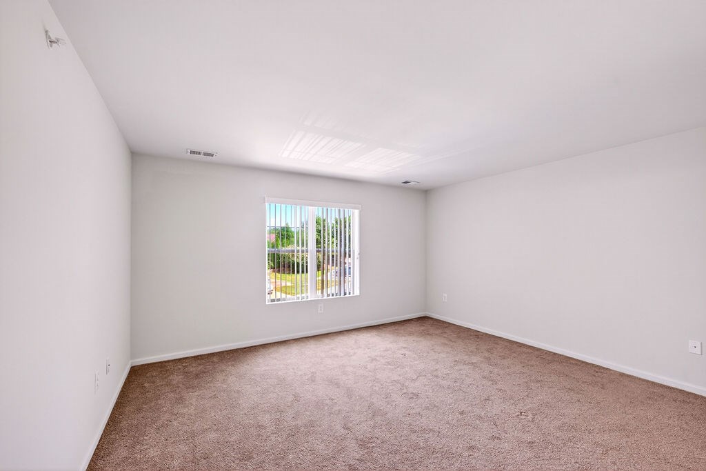 A room with white walls and a window with a view of a fence and trees.
