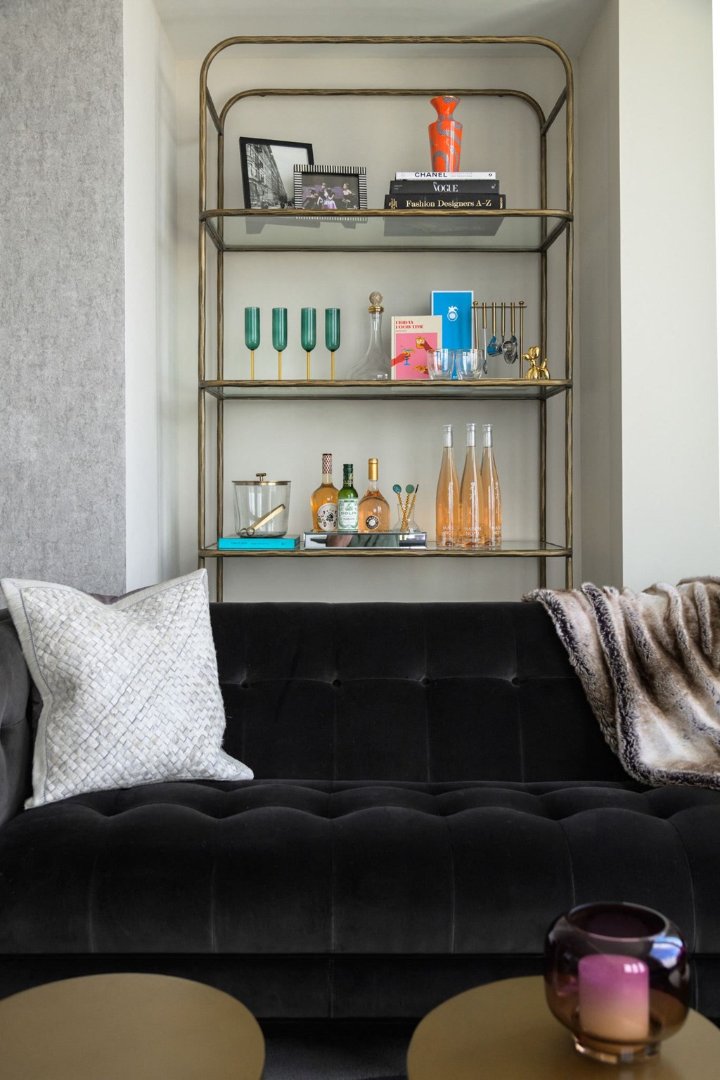 a living room with a black couch and a shelf with bottles and glasses