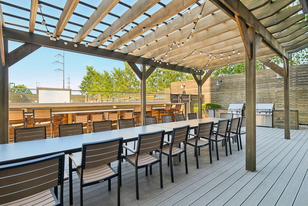 A wooden deck with tables and chairs under a pergola.