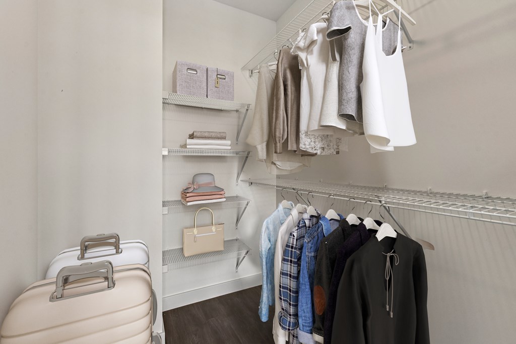 A suitcase is on the floor next to a closet with clothes hanging.