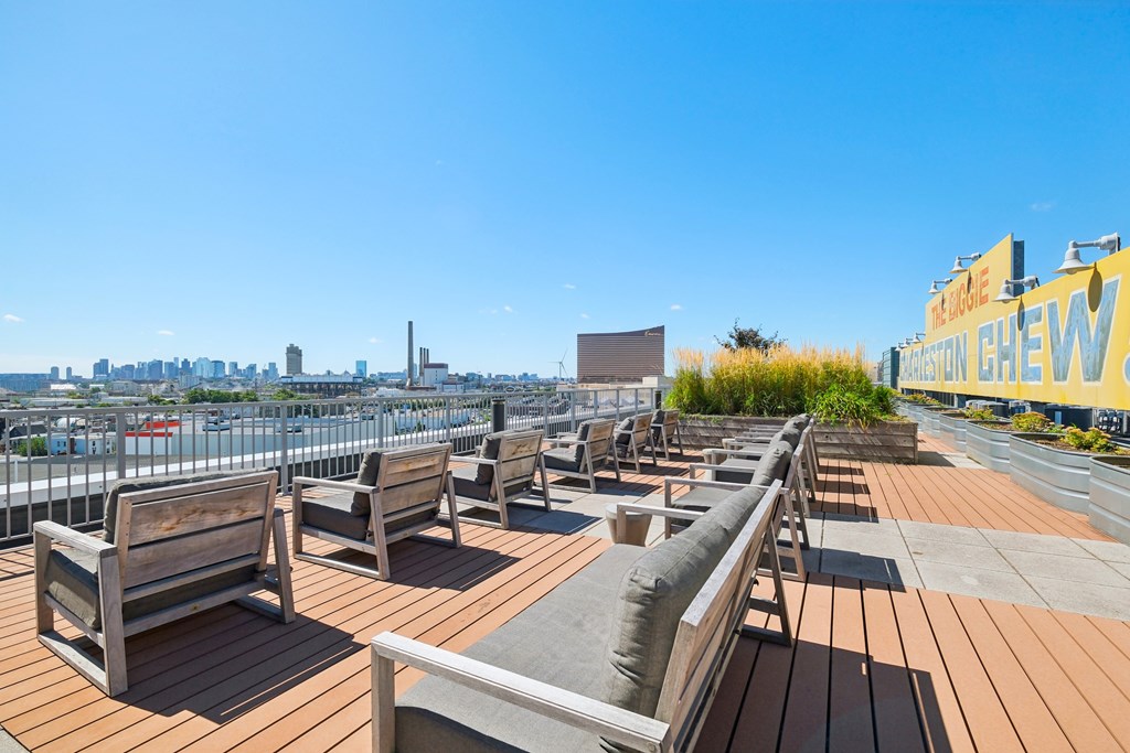 A rooftop patio with wooden benches and a view of the city.